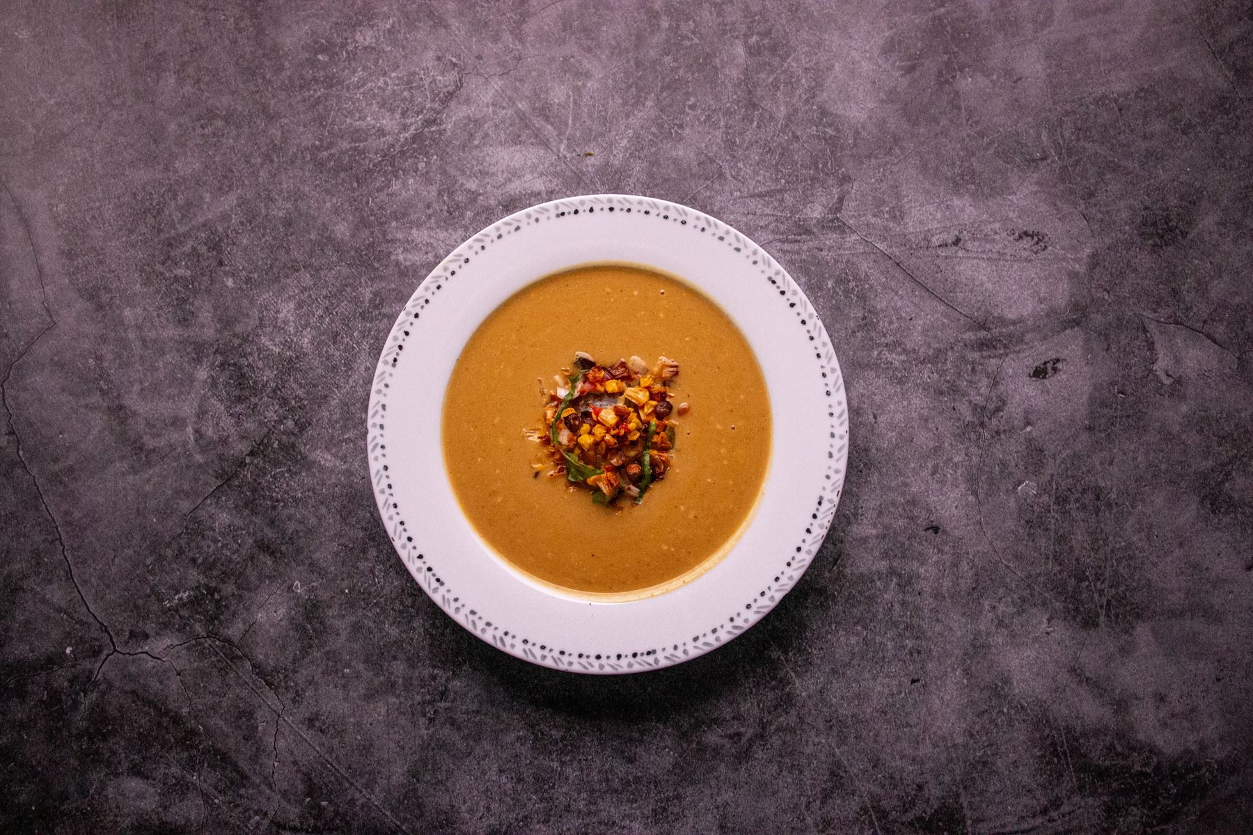Sopa cremosa servida numa tigela, sobre pedra escura